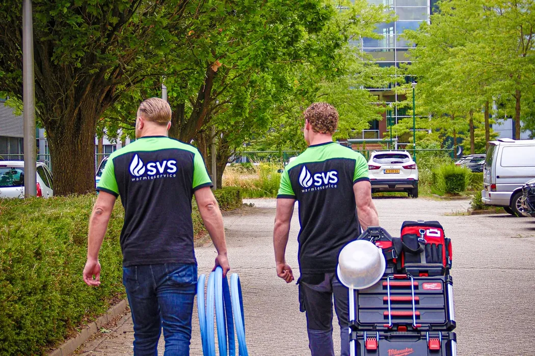 Twee monteurs van SVS Warmteservice lopen met gereedschap naar een appartementencomplex.